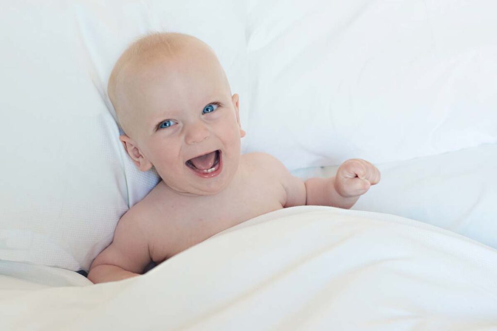 Laughing baby lying under duvet
